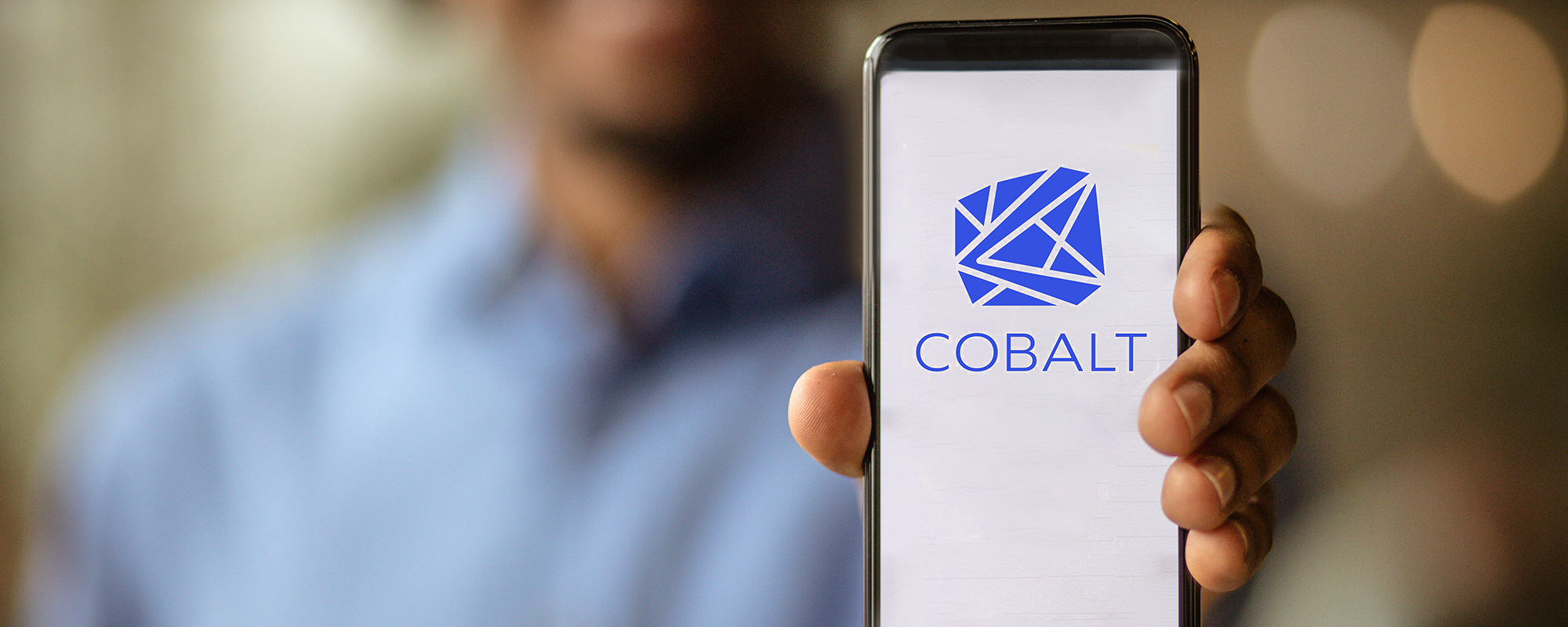 Person holding up a phone with screen displaying "COBALT" and program logo
