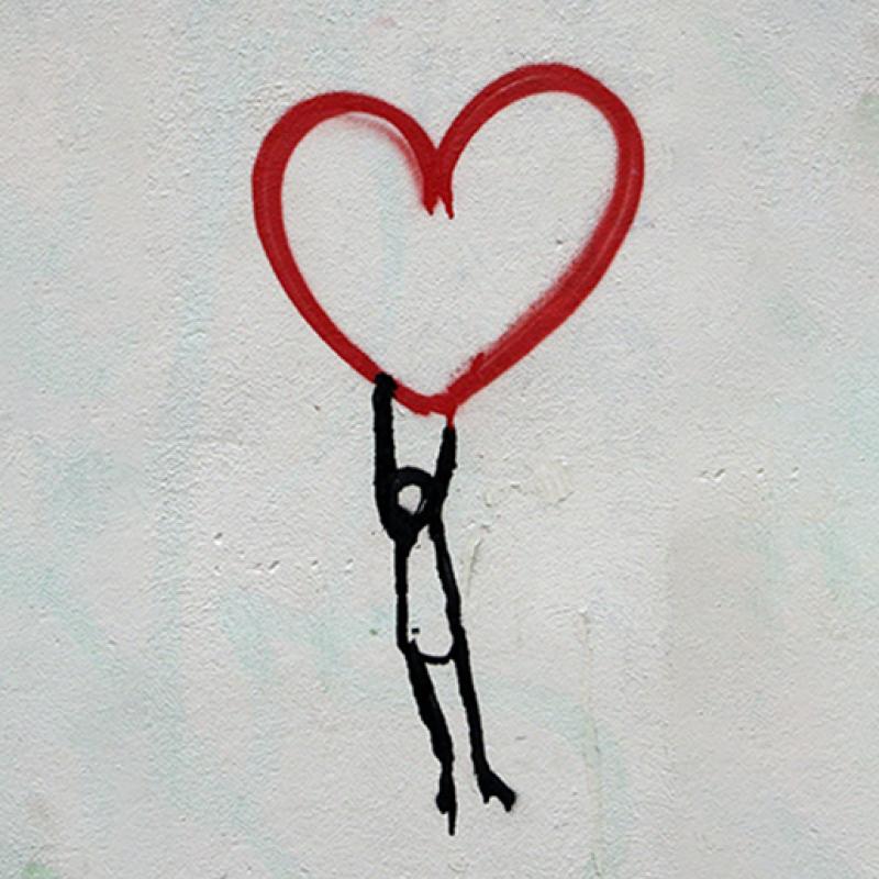Graffiti of an outlined human figure hanging off the bottom of a large red heart