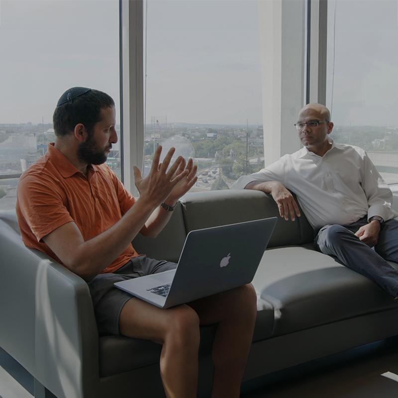 Michael Kopinsky and Mohan Balachandran sit on an office couch and have a conversation