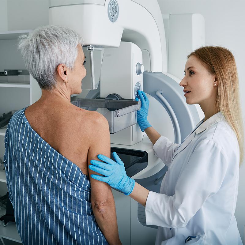 Senior patient and clinician standing next to a mammogram patient