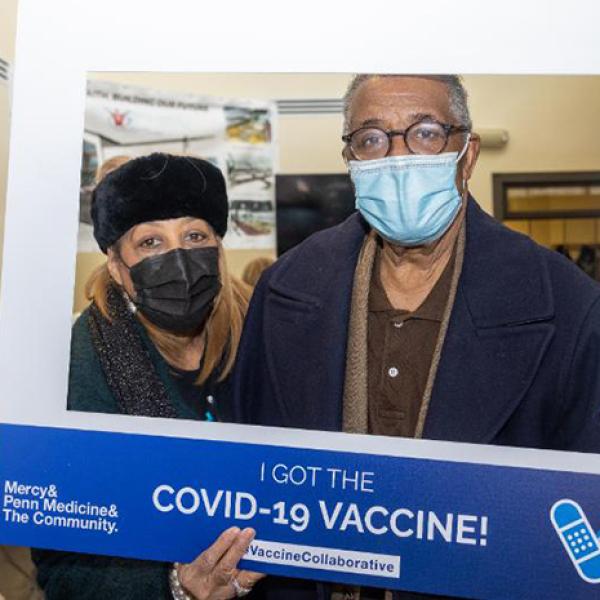 Two people inside a large cardboard frame saying "I got the COVID-19 vaccine!"